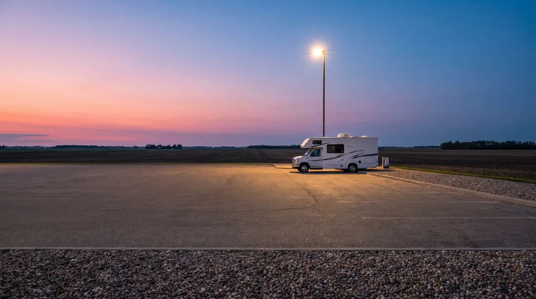 A white motorhome parked alone at the edge of a paved lot on the prairie at dusk.